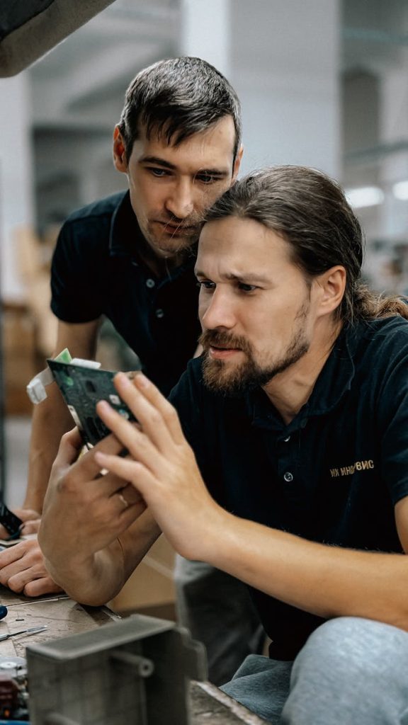 Two engineers closely inspecting a green circuit board for electronic components.